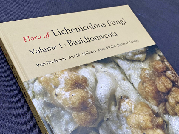 A book lying on a navy blue cloth. On the cover there is a macro photo of a brown, strongly corrugated lichen thallus