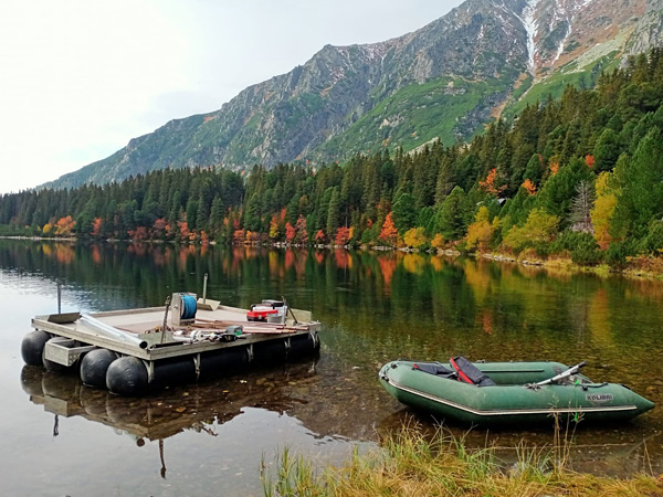 A pond in an autumnal mountain landscape. A platform with research equipment and a pontoon are moored on its shore
