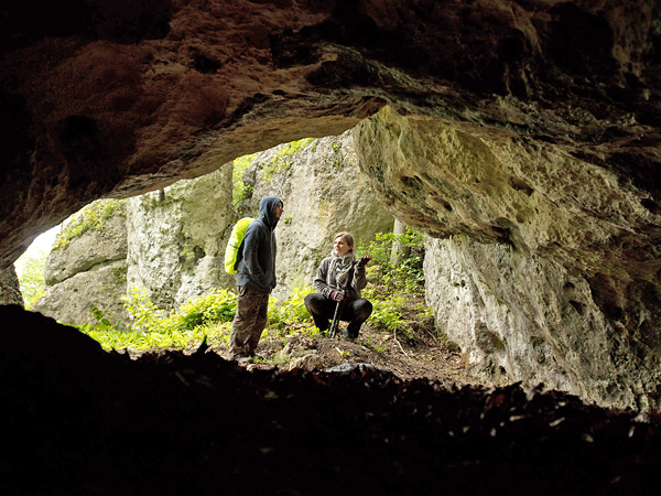 A view from the dark interior of the cave towards the entrance, where two people are having a conversation