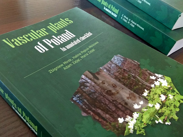 A book lying on a table. In the middle of the green cover there is a photo of anemones cut out in the shape of Poland