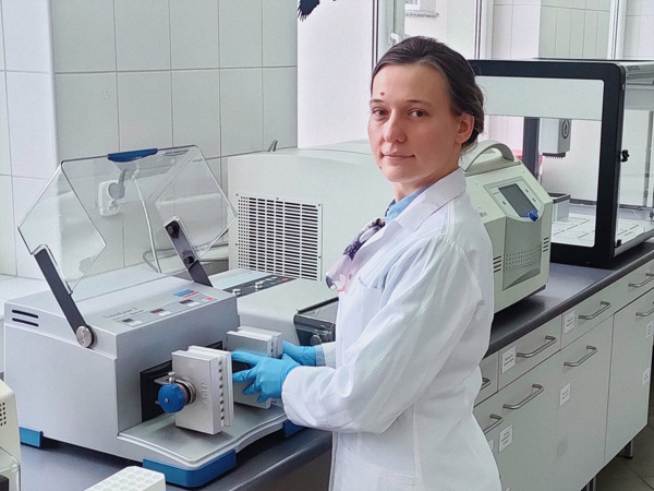 Dark-haired woman in a white lab coat standing in front of a counter with laboratory equipment