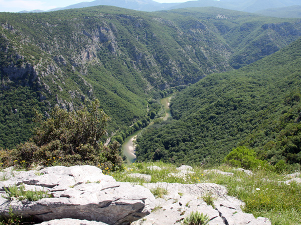 A narrow, winding river cutting through mountainous terrain; on both sides, steep slopes covered with dense forest