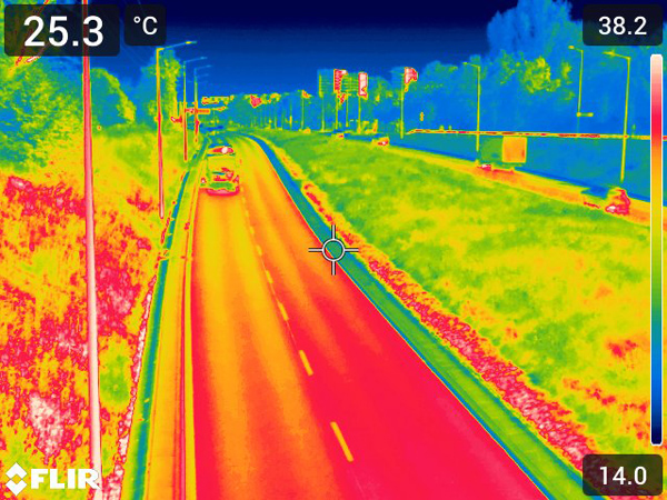 Thermal image of a wide city street; the roadway appears red, while green belts are yellow-green