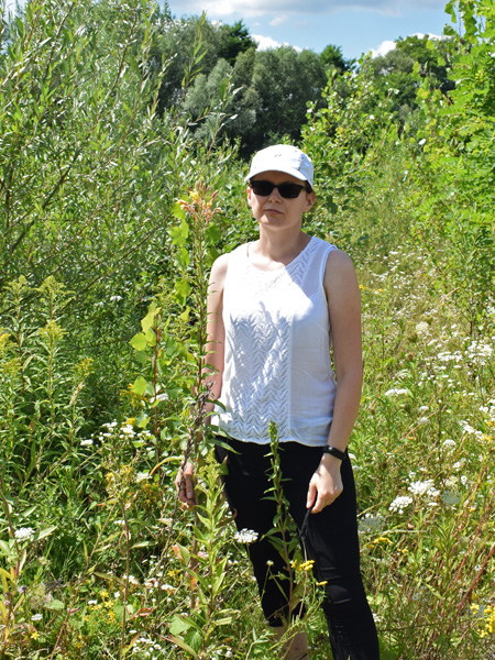 Woman wearing sunglasses and a baseball cap stands in full sunlight among green plants