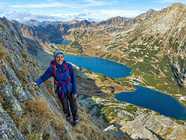 Smiling young woman with a backpack on a mountain trail above a high-mountain valley with three lakes