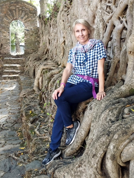 Smiling young woman sits inside ancient ruins; stone wall, steps and a semicircular portal in the background